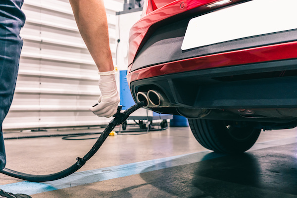 A young technician doing an emission control in a security inspection of a vehicle protected with a mask and gloves