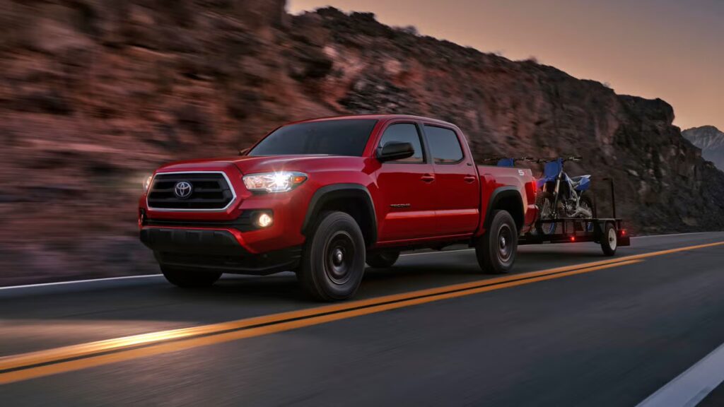 a red 2023 Toyota Tacoma driving near a mountain pulling two bikes behind at sunset.