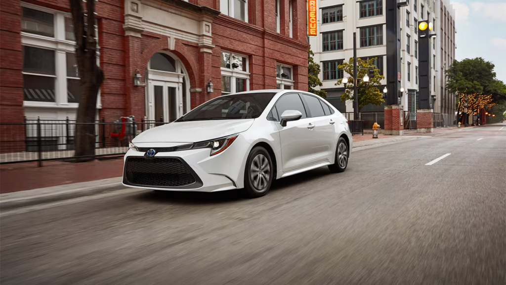 2024 Toyota Corolla Hybrid driving through a city street, showcasing a fuel-efficient and reliable sedan ideal for daily commuting.