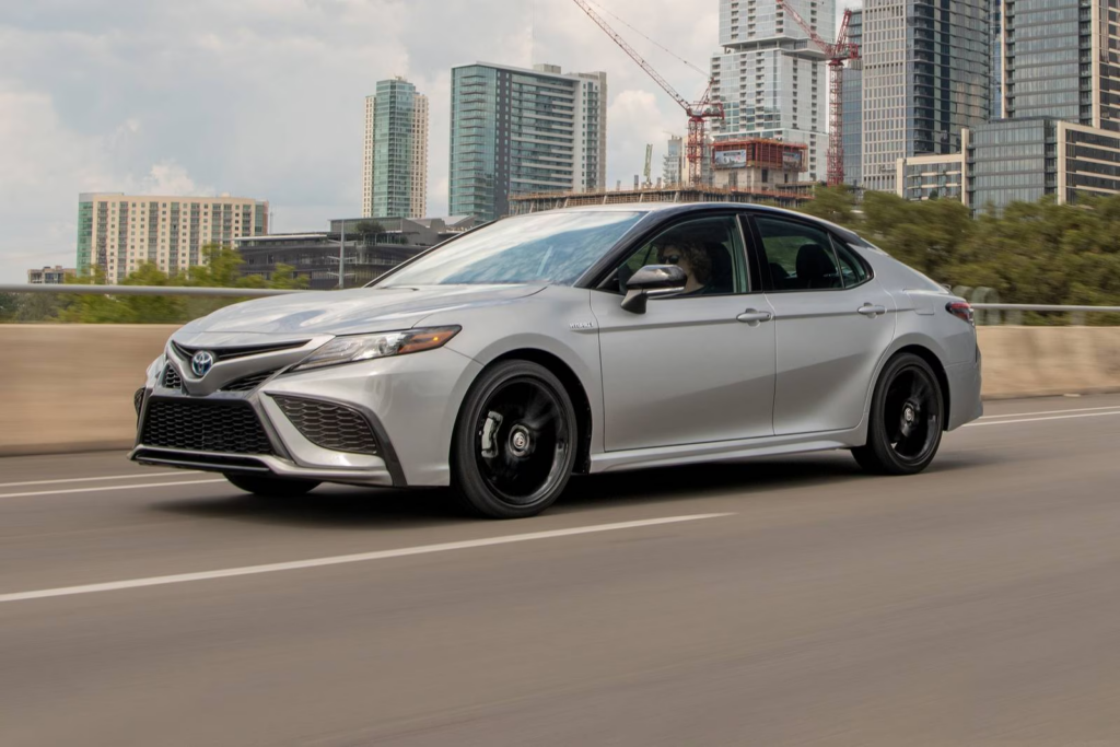 2022 Toyota Camry Hybrid driving on a city highway, showcasing a fuel-efficient and reliable sedan ideal for long daily commutes.