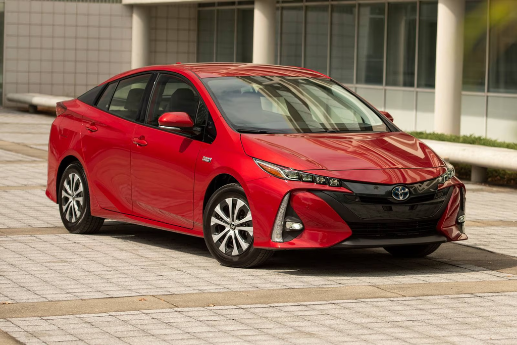 2022 Toyota Prius Prime PHEV in red parked on a paved plaza in front of a modern building.