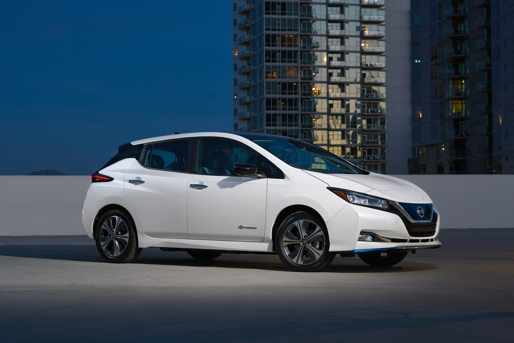 White 2024 Nissan Leaf parked on a rooftop with city buildings in the background.